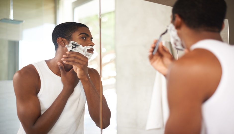 A young man shaving in the mirror